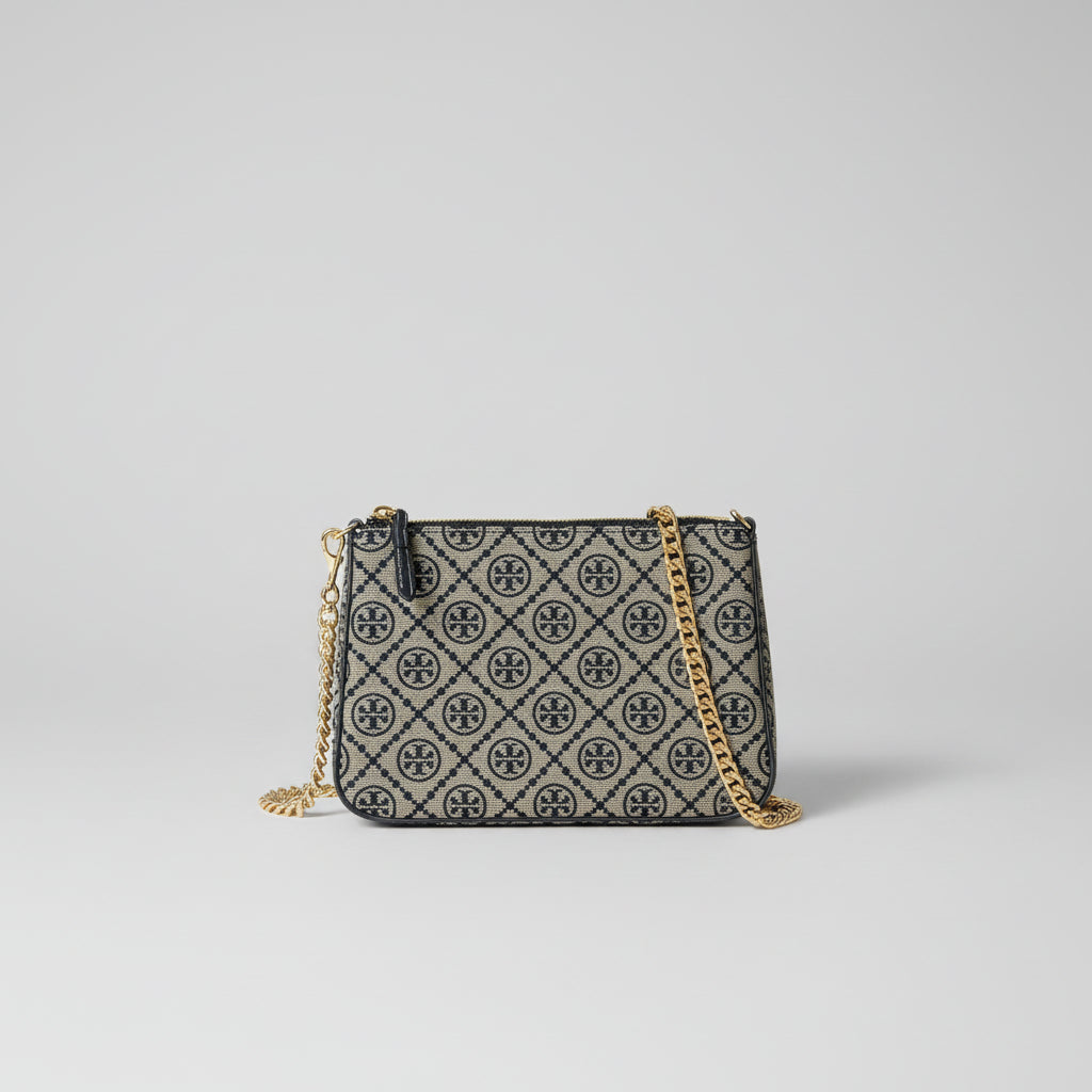 A small patterned handbag with a gold chain strap and gold hardware, placed inside a red box lined with pink tissue paper. The bag has an allover dark monogram pattern on a light beige background.